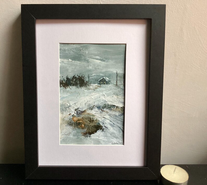 Op de afbeelding: Een olieverfschilderij in een zwarte lijst met een winterlandschap, een klein huisje in de verte, besneeuwde grond en een donkere, bewolkte lucht. Het kunstwerk toont dikke, gestructureerde penseelstreken in tinten wit, grijs en bruin.