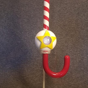 May include: A red and white candy cane shaped Christmas stocking holder with a yellow star and a white base.