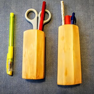 May include: Two wooden pencil holders, one with a red pencil, a pair of scissors, and a yellow pen, and the other with a silver pen, a red pen, and a silver pen.