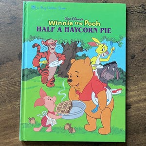 May include: A hardcover children's book titled Walt Disney's Winnie the Pooh Half a Haycorn Pie. The green cover features illustrations of Tigger, Rabbit, Eeyore, Piglet, and Winnie the Pooh holding plates and forks around a pie on a grassy field.