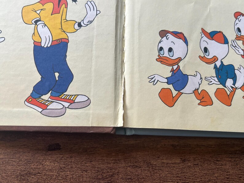 May include: A vintage book page illustration featuring a tall character in a yellow shirt, blue pants, and red sneakers on the left, and two small duck characters wearing blue shirts and orange caps walking on the right against a cream background.