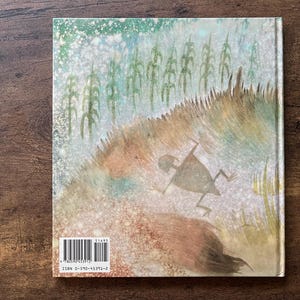 May include: A hardcover book back cover featuring a watercolor illustration of a stylized figure running through a field of tall grass and corn stalks. The artwork uses muted green, brown, and white tones. A barcode and ISBN 0-590-45391-2 are visible.