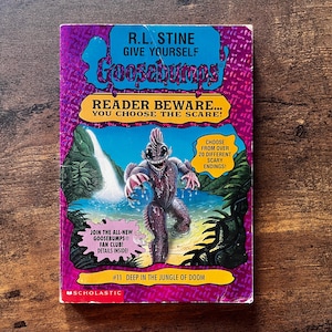 May include: A paperback book titled Give Yourself Goosebumps #11 Deep in the Jungle of Doom by R.L. Stine. The cover features a purple background with a central illustration of a swamp creature in a jungle setting with a waterfall.