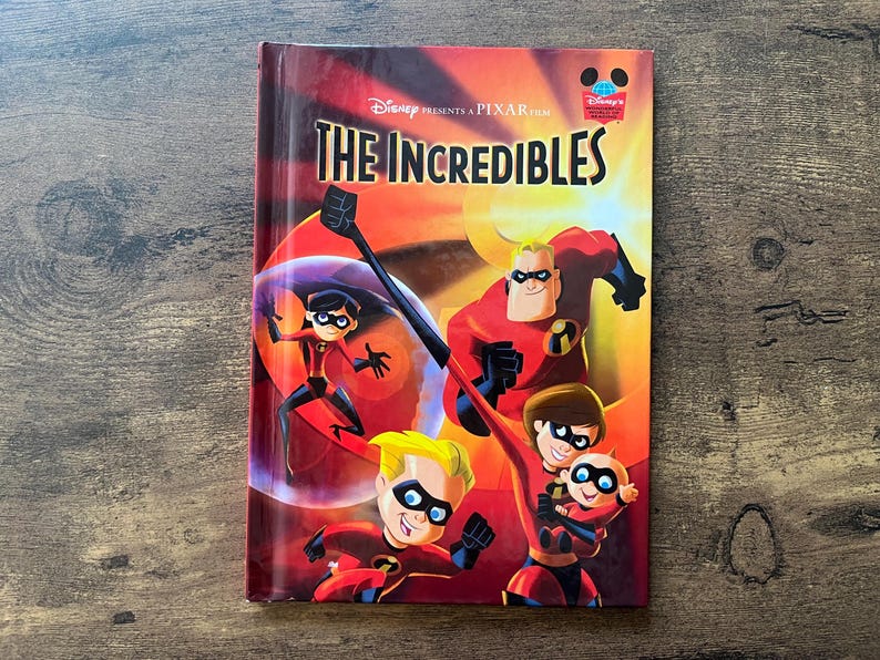May include: A hardcover book titled The Incredibles, featuring a Disney Pixar film logo at the top. The cover displays the animated family of superheroes in their red and black costumes, including Mr. Incredible, Elastigirl, Violet, Dash, and Jack-Jack.