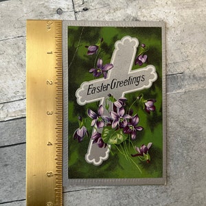May include: Vintage Easter greeting card with a silver cross and purple flowers on a green background. The card reads "Easter Greetings".