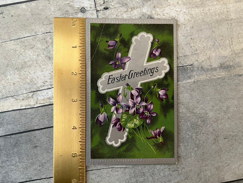 May include: Vintage Easter greeting card with a silver cross and purple flowers on a green background. The card reads "Easter Greetings".