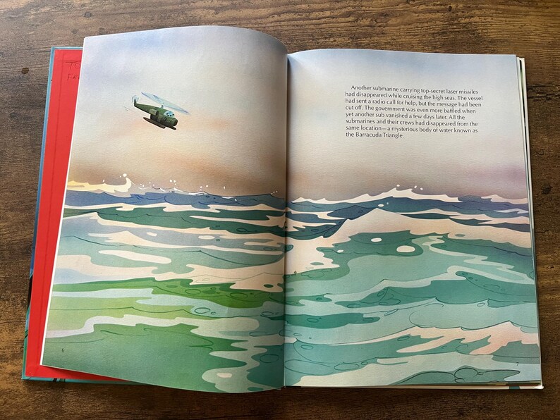 Op de afbeelding: Een open boek met een aquarelillustratie van een groene helikopter die boven een onrustige oceaan met witgekuifde golven vliegt. De rechterpagina bevat gedrukte tekst over een verdwenen onderzee&euml;r in de Barracuda-driehoek.