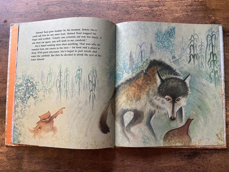 May include: An open children's storybook featuring a watercolor illustration of a coyote and a horned toad in a cornfield. The left page contains printed text about Ma'ii and Horned Toad, while the right page depicts the animals in a field.