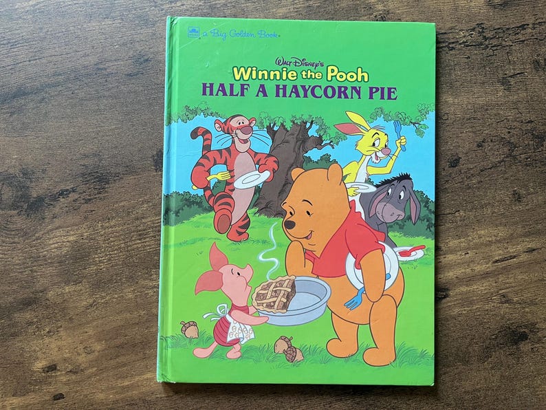 May include: A hardcover children's book titled Walt Disney's Winnie the Pooh Half a Haycorn Pie. The green cover features illustrations of Tigger, Rabbit, Eeyore, Piglet, and Winnie the Pooh holding plates and forks around a pie on a grassy field.