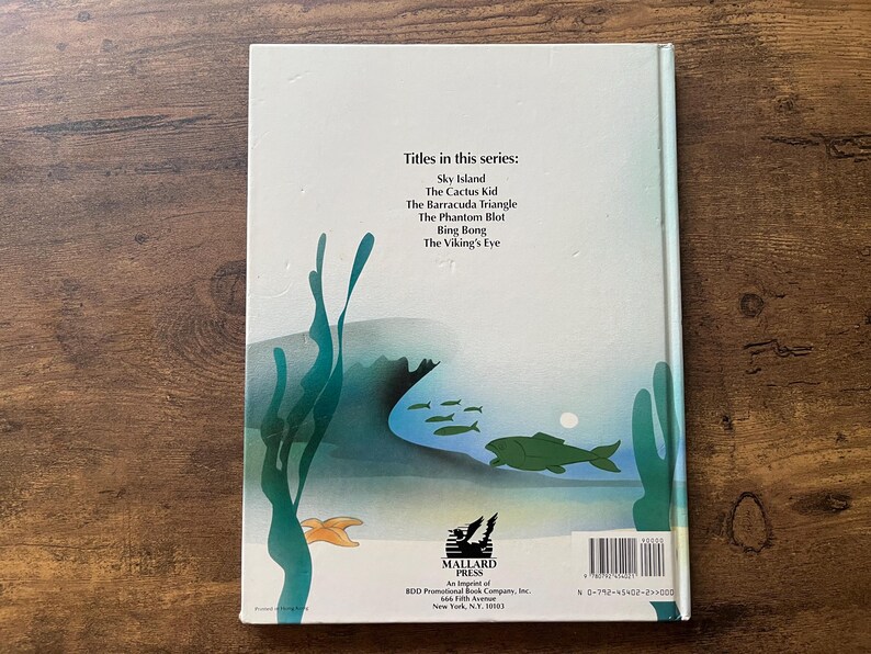 Op de afbeelding: Een lichtgekleurde boekomslag met een onderwaterillustratie met groen zeewier, een grote groene vis, kleinere vissen en een zeester. De tekst luidt: Titles in this series: Sky Island, The Cactus Kid, The Barracuda Triangle, The Phantom Blot, Bing Bong, The Viking's Eye en Mallard Press.