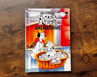 May include: A hardcover book titled Walt Disney's 101 Dalmatians featuring a colorful illustration of adult and puppy Dalmatians in a basket in front of a fireplace. The title text is printed in large black and white spotted lettering.
