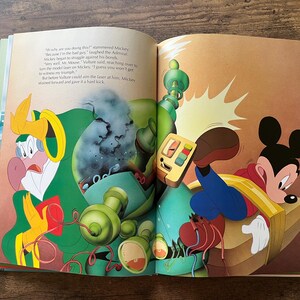 Op de afbeelding: Een open kinderboek met een kleurrijke illustratie van Mickey Mouse in een rood shirt en blauwe broek, vastgebonden aan een houten platform, terwijl een in het groen gekleed vogelachtig figuur met een mechanisch apparaat ernaast staat.