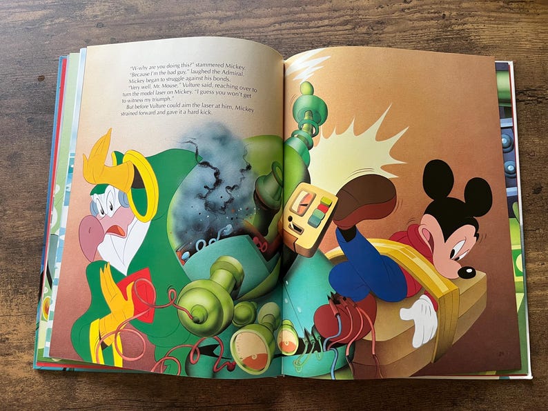 Op de afbeelding: Een open kinderboek met een kleurrijke illustratie van Mickey Mouse in een rood shirt en blauwe broek, vastgebonden aan een houten platform, terwijl een in het groen gekleed vogelachtig figuur met een mechanisch apparaat ernaast staat.
