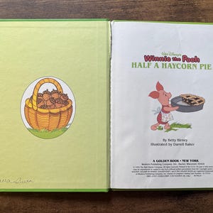 Puede incluir: Un libro infantil de tapa dura titulado Walt Disney's Winnie the Pooh Half a Haycorn Pie. La p&aacute;gina izquierda muestra una cesta amarilla llena de bellotas marrones. La p&aacute;gina derecha muestra a Piglet sosteniendo un pastel, con texto de Betty Birney e ilustraciones de Darrell Baker.