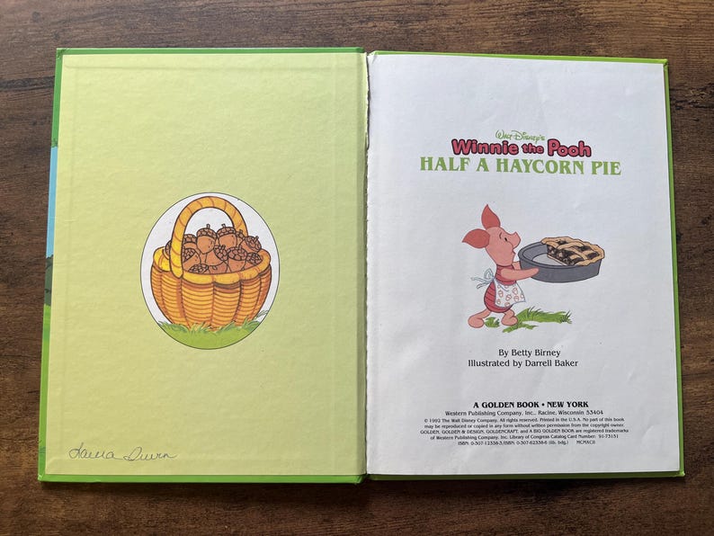 Puede incluir: Un libro infantil de tapa dura titulado Walt Disney's Winnie the Pooh Half a Haycorn Pie. La p&aacute;gina izquierda muestra una cesta amarilla llena de bellotas marrones. La p&aacute;gina derecha muestra a Piglet sosteniendo un pastel, con texto de Betty Birney e ilustraciones de Darrell Baker.