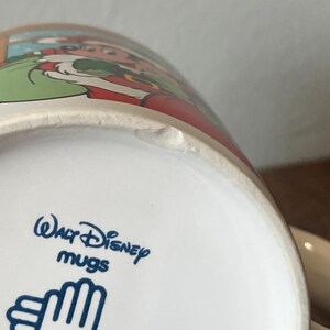 Puede incluir: Taza de cer&aacute;mica blanca con una colorida ilustraci&oacute;n de un personaje de dibujos animados. La taza tiene el texto "Walt Disney mugs" en azul. La taza es blanca con una peque&ntilde;a astilla en el borde.