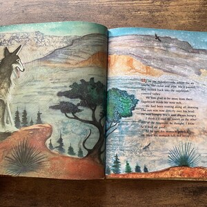 May include: An open children's book featuring a watercolor illustration of a coyote sitting on a rocky ledge overlooking a valley. The right page contains printed text describing the scene, with a mountain landscape and trees in the background.