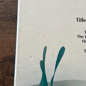 Op de afbeelding: Een witte boekomslag met een lijst van titels waaronder Sky Island, The Cactus, The Barracuda, The Phantom, Bing B en The Viking. Onder de tekst staat een gestileerde, blauwgroene grafische illustratie van waterplanten of zeewier.