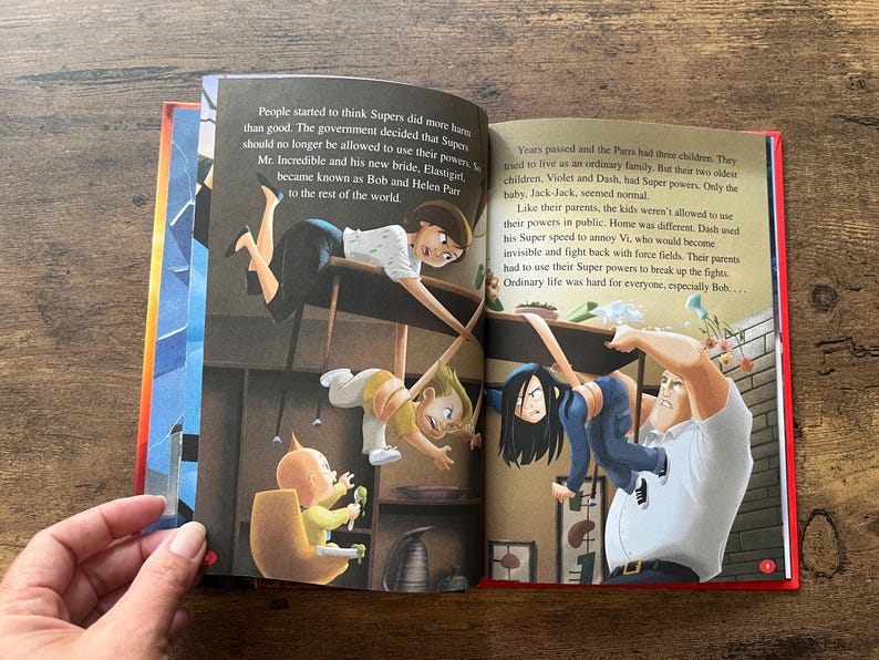 May include: An open children's storybook featuring The Incredibles characters. The left page shows a woman and a baby in a high chair, while the right page depicts a man holding a girl. Both pages contain printed English text narrating the story.