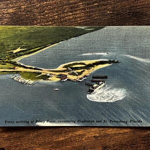 May include: A vintage postcard featuring an aerial view of a ferry arriving at Piney Point, Florida. The image shows a ferry boat in blue water, a sandy shoreline, and green land. The text reads: Ferry arriving at Piney Point, connecting Bradenton and St. Petersburg, Florida.