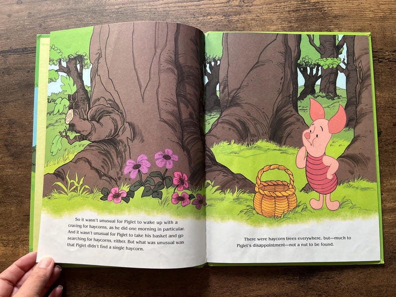 Puede incluir: Una p&aacute;gina de libro infantil abierta con una ilustraci&oacute;n colorida de Piglet de pie en un bosque junto a una cesta tejida. El texto dice: So it wasn't unusual for Piglet to wake up with a craving for haycorns, y There were haycorn trees everywhere, but&mdash;much to Piglet's disappointment&mdash;not a nut to be found.