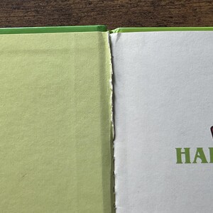 Puede incluir: Un primer plano de un libro abierto con una cubierta de color verde claro y p&aacute;ginas blancas. El lomo interior muestra signos de desgaste con bordes de papel deshilachados. En la p&aacute;gina derecha, el texto "Win" en rojo y "HALF A" en verde.
