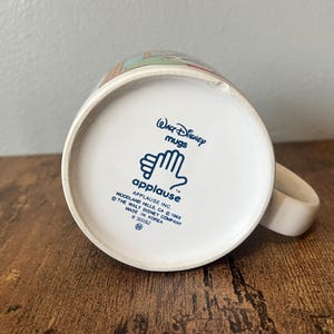 Puede incluir: Taza de cer&aacute;mica blanca de Disney con asa. La base de la taza presenta el texto "Walt Disney Mugs" y "applause" con un logotipo de mano. La taza est&aacute; hecha en Corea.