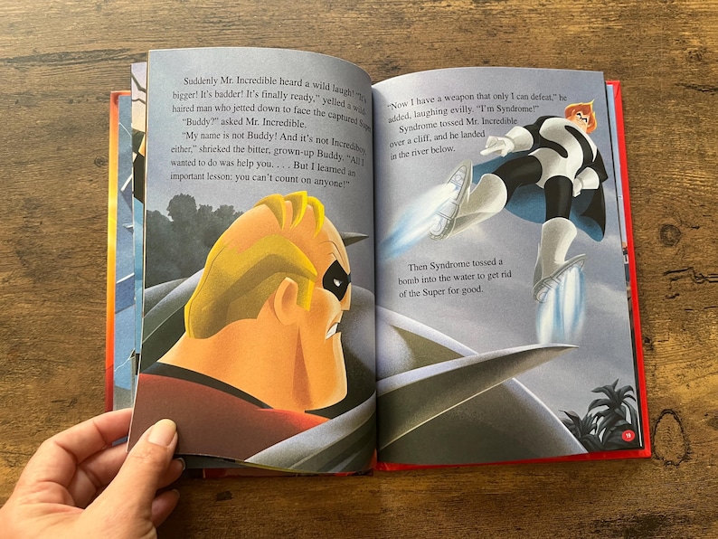 May include: An open children's storybook featuring a scene from The Incredibles. The left page shows Mr. Incredible in profile, while the right page depicts the character Syndrome flying with rocket boots above water, accompanied by printed narrative text.