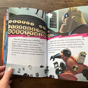 May include: An open children's storybook featuring illustrations of Mr. Incredible from The Incredibles. The left page shows a computer keyboard with the text KRONOS, while the right page depicts Mr. Incredible in his red and black suit.