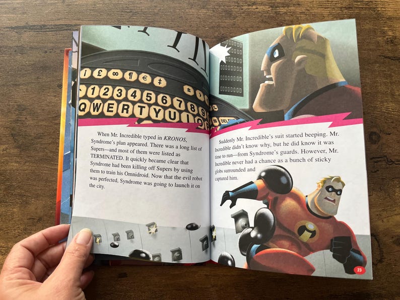 May include: An open children's storybook featuring illustrations of Mr. Incredible from The Incredibles. The left page shows a computer keyboard with the text KRONOS, while the right page depicts Mr. Incredible in his red and black suit.