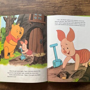 Puede incluir: Un libro de cuentos infantil abierto con Winnie the Pooh y Piglet. La p&aacute;gina izquierda muestra a los personajes cerca de una casa en el &aacute;rbol, mientras que la derecha muestra a Piglet plantando una bellota con una pala azul. Texto incluido.