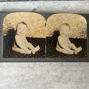 Puede incluir: Una tarjeta estereoscópica vintage con una imagen en blanco y negro de un bebé sentado en una alfombra estampada. La tarjeta tiene texto en la parte inferior que dice "Just as Gold" y texto en el lateral que dice "Keystone View Company, Manufacturers, Publishers, Copyright 1917 by R. Lebinglag, NY London England".