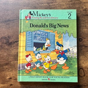 May include: A vintage copy of "Donald's Big News," a Walt Disney book for young readers. The cover features Donald Duck and his nephews, with a blue window and green background. The book is part of Mickey's Young Readers Library, Volume 2.