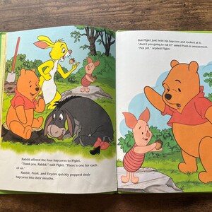 Puede incluir: Un libro de cuentos infantil abierto con ilustraciones coloridas de Winnie the Pooh, Piglet, Igor y Conejo. Las p&aacute;ginas muestran a los personajes en un bosque con texto que describe una escena donde comparten bellotas de heno.