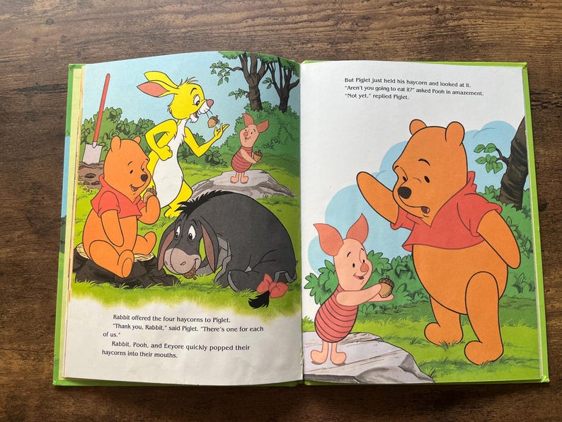 Puede incluir: Un libro de cuentos infantil abierto con ilustraciones coloridas de Winnie the Pooh, Piglet, Igor y Conejo. Las p&aacute;ginas muestran a los personajes en un bosque con texto que describe una escena donde comparten bellotas de heno.