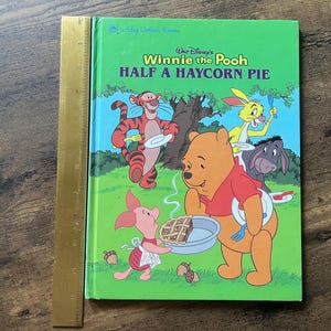 Puede incluir: Un libro de tapa dura Big Golden Book titulado Walt Disney's Winnie the Pooh Half a Haycorn Pie, con ilustraciones de Pooh, Piglet, Tigger, Rabbit y Eeyore. Una regla dorada de 30 cm est&aacute; colocada verticalmente a lo largo del lado izquierdo.