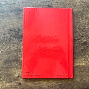 May include: A rectangular book with a solid, glossy red cover. The bottom left corner features the text Scholastic Inc. and a small paragraph of text, while the bottom right corner displays the ISBN number 0-7172-7751-9 in black font.