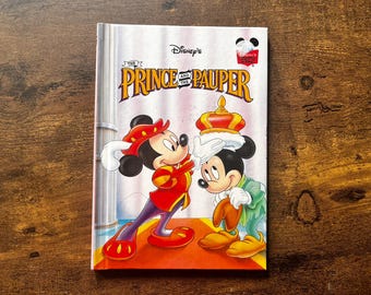 May include: A hardcover book titled Disney's The Prince and the Pauper featuring an illustration of two Mickey Mouse characters on the cover. One character wears a red and gold royal outfit and places a golden crown on the other character's head.