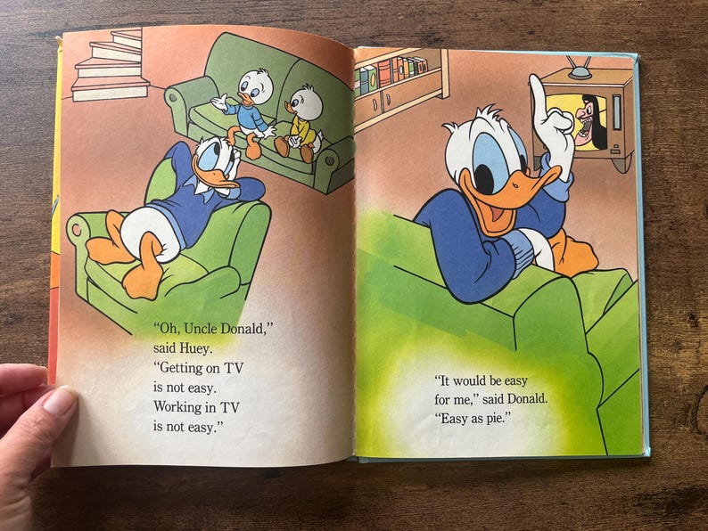 May include: An open children's book page featuring Donald Duck and his nephews in a living room. The text reads: Oh, Uncle Donald, Getting on TV is not easy. Working in TV is not easy. It would be easy for me, said Donald. Easy as pie.