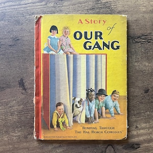 May include: A vintage copy of "Our Gang" book with a yellow cover. The cover features illustrations of children and a dog, with the title "A Story of Our Gang" in large letters. The book also includes the text "Romping Through The Hal Roach Comedies."