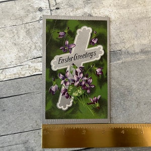 May include: Vintage Easter greeting card with a silver cross and purple flowers on a green background. The card reads "Easter Greetings".