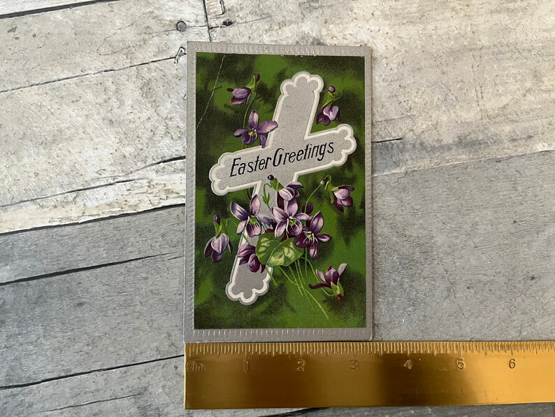 May include: Vintage Easter greeting card with a silver cross and purple flowers on a green background. The card reads "Easter Greetings".