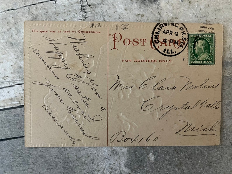 May include: A vintage postcard with a floral design. The postcard is addressed to Miss Clara Murlin in Crystal Falls, Michigan. The postcard has a 1-cent stamp from the United States Post Office dated April 9, 1911.