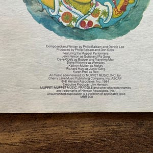 May include: A printed paper insert featuring a colorful illustration of a character at the top and black text detailing credits for a production. The text lists Philip Balsam, Dennis Lee, and various Muppet performers, dated 1984 by Henson Associates.