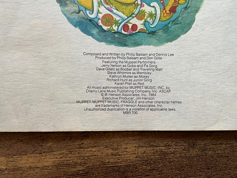 May include: A printed paper insert featuring a colorful illustration of a character at the top and black text detailing credits for a production. The text lists Philip Balsam, Dennis Lee, and various Muppet performers, dated 1984 by Henson Associates.