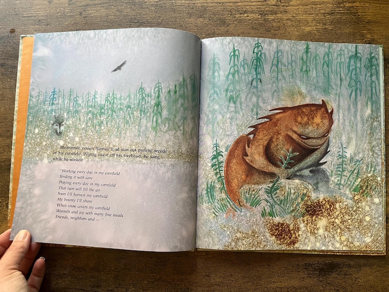 May include: An open children's book featuring a brown, horned toad creature sitting in a green cornfield. The left page contains printed text about a horned toad working in a cornfield, while the right page shows the creature in a field.