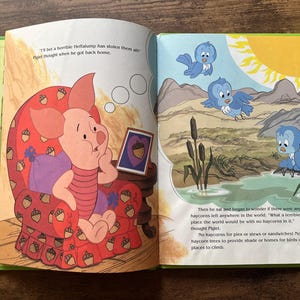 Puede incluir: Un libro infantil abierto que muestra a Piglet sentado en un sill&oacute;n rojo con estampado de bellotas. La p&aacute;gina izquierda muestra a Piglet pensando, mientras que la derecha ilustra un paisaje con p&aacute;jaros azules, un estanque y juncos bajo un sol amarillo brillante.