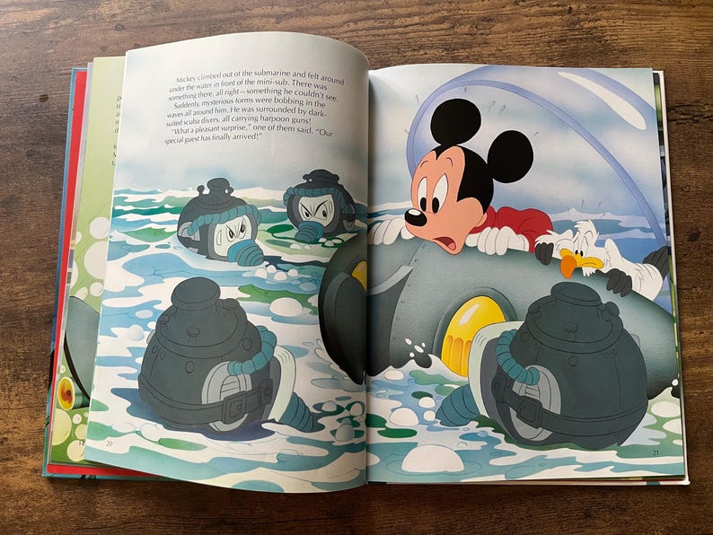 Op de afbeelding: Een open kinderboek met een kleurrijke illustratie van Mickey Mouse in een grijze onderzee&euml;r, omringd door donkergekleurde duikers in het water. De tekst op de linkerpagina beschrijft hoe Mickey uit de onderzee&euml;r klimt.