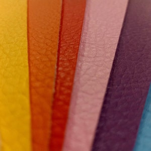 May include: Close-up of a rainbow of leather strips, showing the texture of the material. The colors are beige, yellow, orange, red, pink, purple, and blue.
