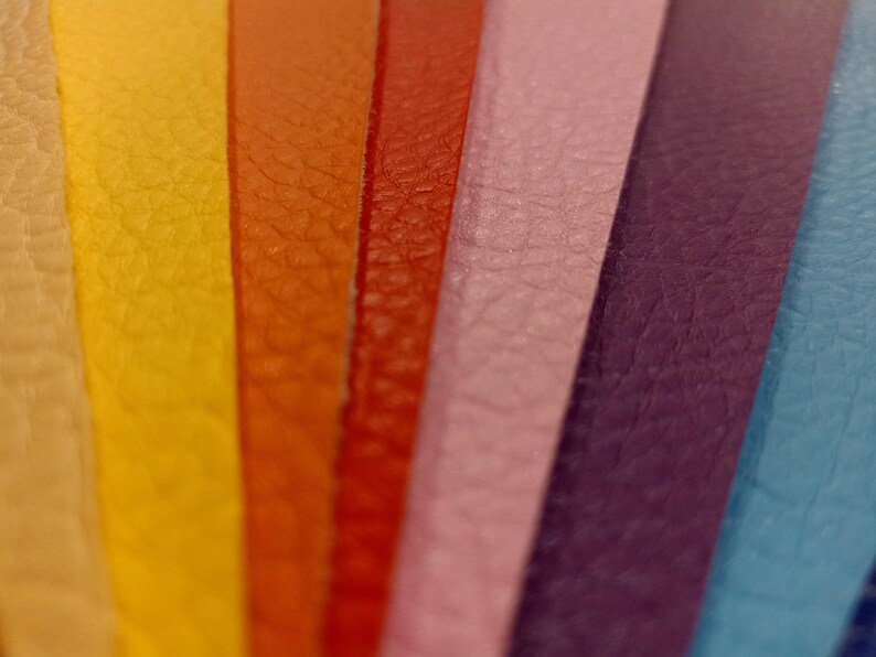 May include: Close-up of a rainbow of leather strips, showing the texture of the material. The colors are beige, yellow, orange, red, pink, purple, and blue.